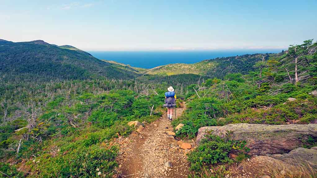 A backpacker hiking along the Green Gardens Trail with coastal views in Gros Morne National Park, Newfoundland, Canada.
